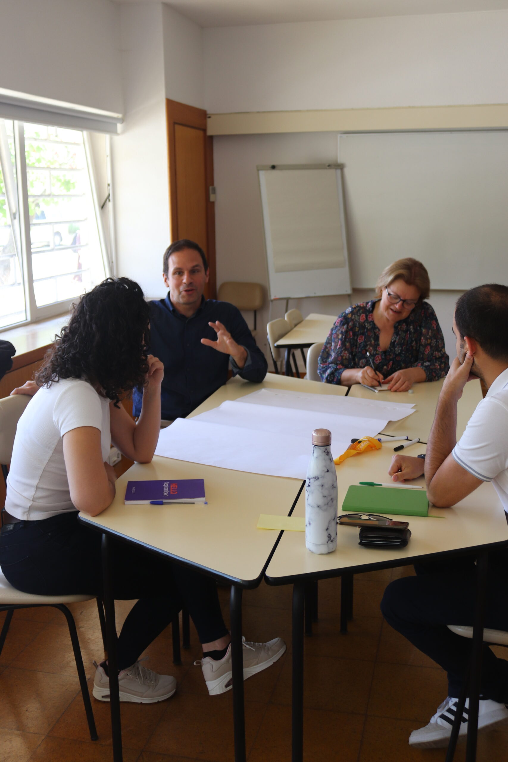 Four participants of the workshop "Workshop: what we want to make visible" sitting in a circle, with an A0 sheet of paper on the table, discussing communication messages.